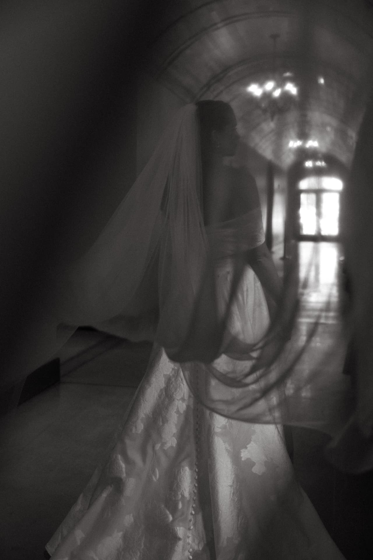 Bride in a lace gown walking down a sunlit hallway